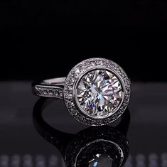 a white gold ring with a round diamond center surrounded by pave diamonds on a reflective surface