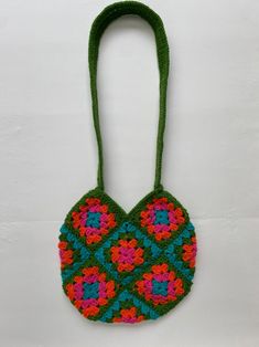 a crocheted bag hanging from a hook on a white wall with a green handle