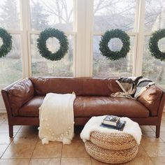 a brown leather couch sitting in front of two large windows with wreaths on them