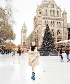 a woman is skating on an ice rink in front of a large building with a christmas tree