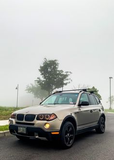 an suv is parked on the side of the road in front of some trees and fog