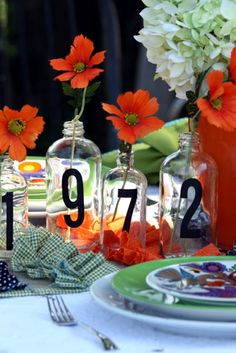 the table is set with orange flowers and glass bottles