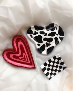 two heart shaped cookies sitting next to each other on a white sheet with black and red designs