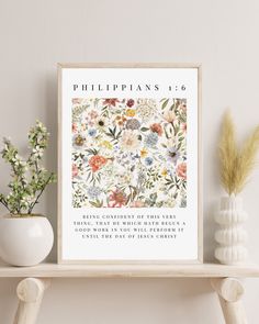 a white vase with flowers on it next to a framed bible verse print that reads, philippians 1 6