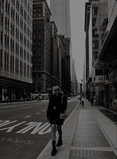 a woman is walking down the sidewalk in front of some tall buildings on a city street