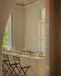 a long table with white linens and yellow place settings in front of a window