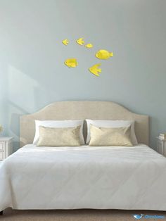 a white bed sitting next to a wall with yellow fish on it's headboard