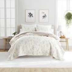 a bed with white comforter and pillows in a room next to two pictures on the wall