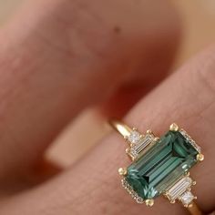 a woman's engagement ring with an emerald and diamond set in yellow gold, on her finger