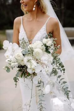 a bride holding a bouquet of white flowers and greenery