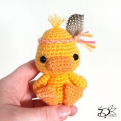 a small crocheted bird with a feather on it's head sitting in someones hand