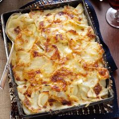 a casserole dish with potatoes and cheese on a table next to wine glasses