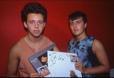 two young men posing for a photo holding up pictures and an autographed card