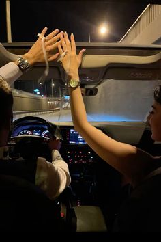 two people sitting in a car with their hands up to each other as they drive