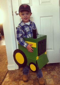 a young boy wearing a tractor costume standing in front of a door with a cardboard box