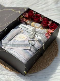 an open box with clothes and flowers in it sitting on a white bedding sheet