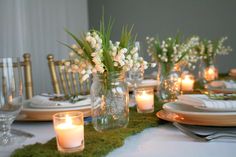 the table is set with candles and flowers in mason jar vases on mossy place mats