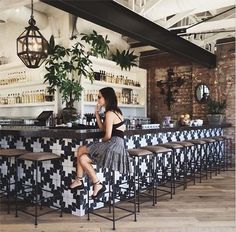 a woman sitting at a bar in front of an open air bar with stools