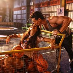 a man kissing a woman in front of a cage with basketballs on the ground