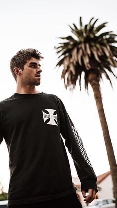 a man standing in front of a palm tree wearing a black shirt with white stripes on the sleeves