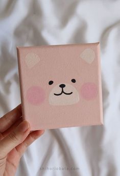 a hand holding up a pink square with a bear face painted on it's side