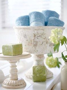 a white bowl filled with blue towels next to two small candles and a vase full of flowers