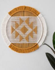 a white and yellow woven wall hanging next to a potted plant on a table