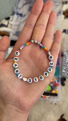 a hand holding a beaded bracelet with words written on it in different colors and shapes