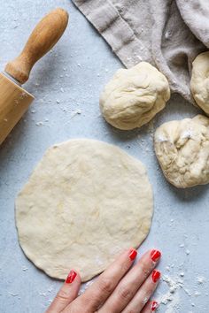 a woman's hand on top of dough next to rolling pin