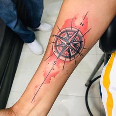 a person with a compass tattoo on their arm and hand is holding a red watercolor stain