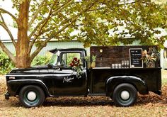 an old black truck with flowers on the back is parked in front of a tree