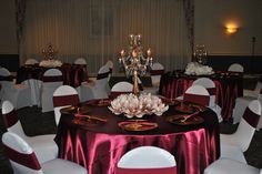 a banquet room set up with white chairs and red table cloths, centerpieces and flowers