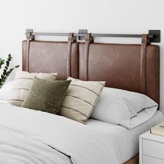 a bed with white sheets and brown headboard, next to a plant on the nightstand