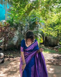 a woman in a blue and purple sari is standing by some trees with her hands on her hips