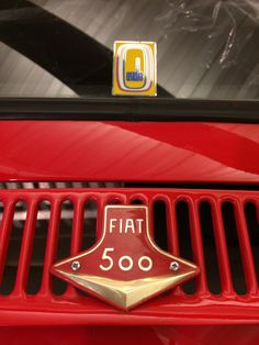 the emblem on the front grille of a red sports utility vehicle with gold trim and letters that read, fiat 500