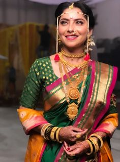 a woman in a green and yellow sari with gold jewelry on her neck, smiling at the camera