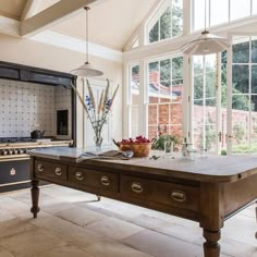 a kitchen with an island, stove and table in front of large windows that look out onto the backyard