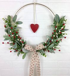 a christmas wreath hanging on a wall with a red heart in the middle and greenery around it