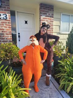 two people dressed in costumes standing on the front steps of a house with plants around them