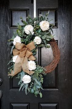 a wreath with white flowers and greenery is hanging on a black front door,