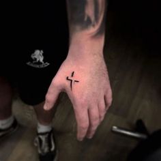 a person with a small cross tattoo on their left hand and the other hand is pointing towards the camera