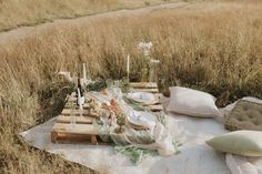 an outdoor picnic setting on a blanket in the middle of a field with flowers and candles