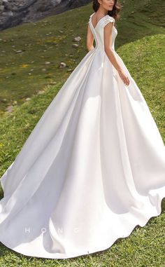 a woman in a white wedding dress standing on the grass with her hands behind her back