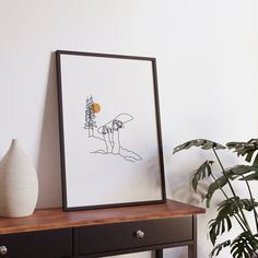 a black and white drawing sitting on top of a wooden table next to a potted plant