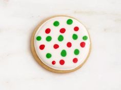 a cookie decorated with red, green and white polka dot icing on a white surface