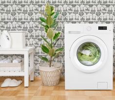 a white washer sitting on top of a wooden floor next to a potted plant