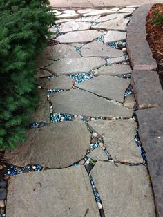 a stone path with blue and white glass beads on the stones, next to a green bush