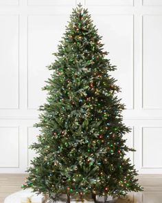 a christmas tree with lights and presents on the floor in front of a white wall