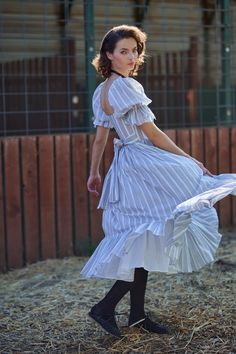 Embrace the spirit of the Old West in this high-waist midi dress, boasting a pleated puff skirt and a playfully ruffled hem. Crafted with bows at the sleeve and waistline, and complete with pockets, it's the perfect attire for singing cowboy ballads while watching the sun set over the prairie. Cotton gauze midi dress with puff sleeves Pleated puff skirt and ruffled hem Side seam pockets Bow tie detail at waist Invisible zipper closure To ensure the best fit, measure your across bust and high wai Spring Midi Dress With Pleated Waist And Voluminous Skirt, Voluminous Full Skirt Dress For Garden Party, Tiered Puff Sleeve Dress With Ruffles For Daywear, Fitted Ruffle Midi Dress For Daywear, Fitted Ruffled Skirt Dresses For Daywear, Fitted Daywear Dresses With Ruffled Skirt, Fitted Dresses With Ruffled Skirt For Daywear, Daywear Puff Sleeve Dress With Tiered Skirt And Ruffles, Daywear Puff Sleeve Tiered Dress With Ruffles