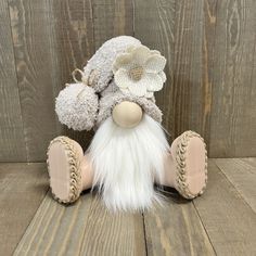 a small stuffed animal with white fur and a flower on it's head, sitting on a wooden surface